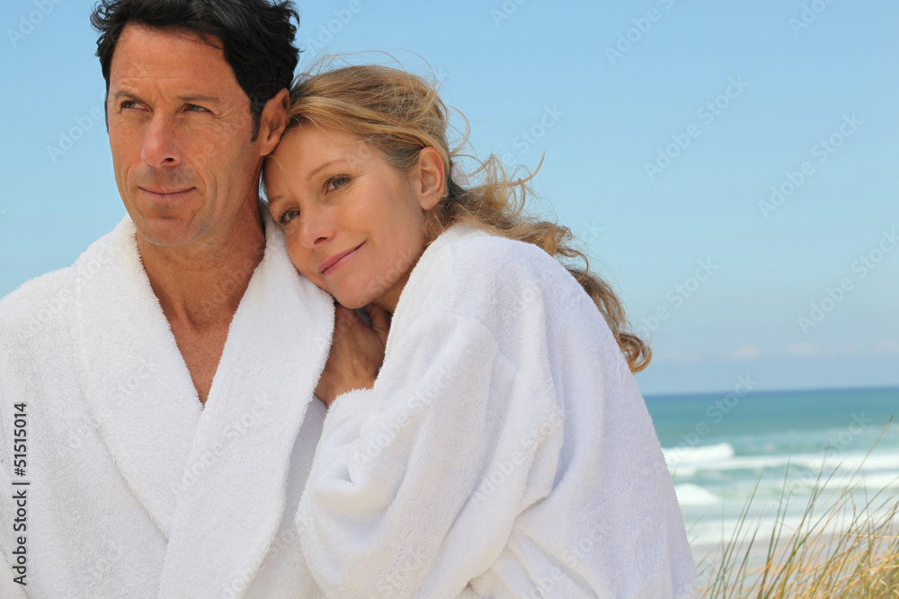 Couple stood on beach wearing bath gowns Couple stood on beach wearing bath gowns