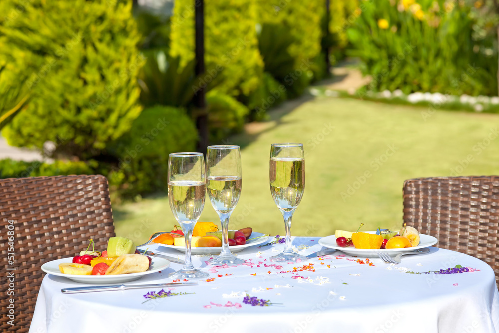 Celebration for three in a garden, fruits and champagne.