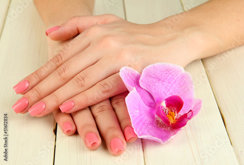 Woman hands with pink manicure and orchid on  wooden background