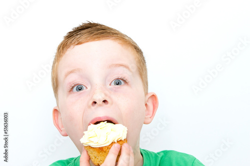 handsome little boy eating a fresh cream cup cake with messy fac