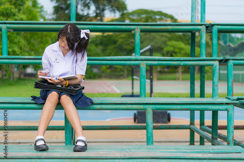 Cute Thai schoolgirl is sitting and reading on a stand.