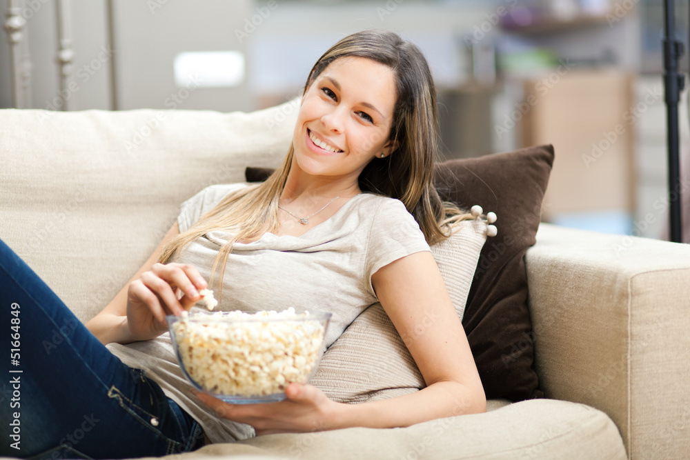 Beautiful young woman eating popcorn on the sofa