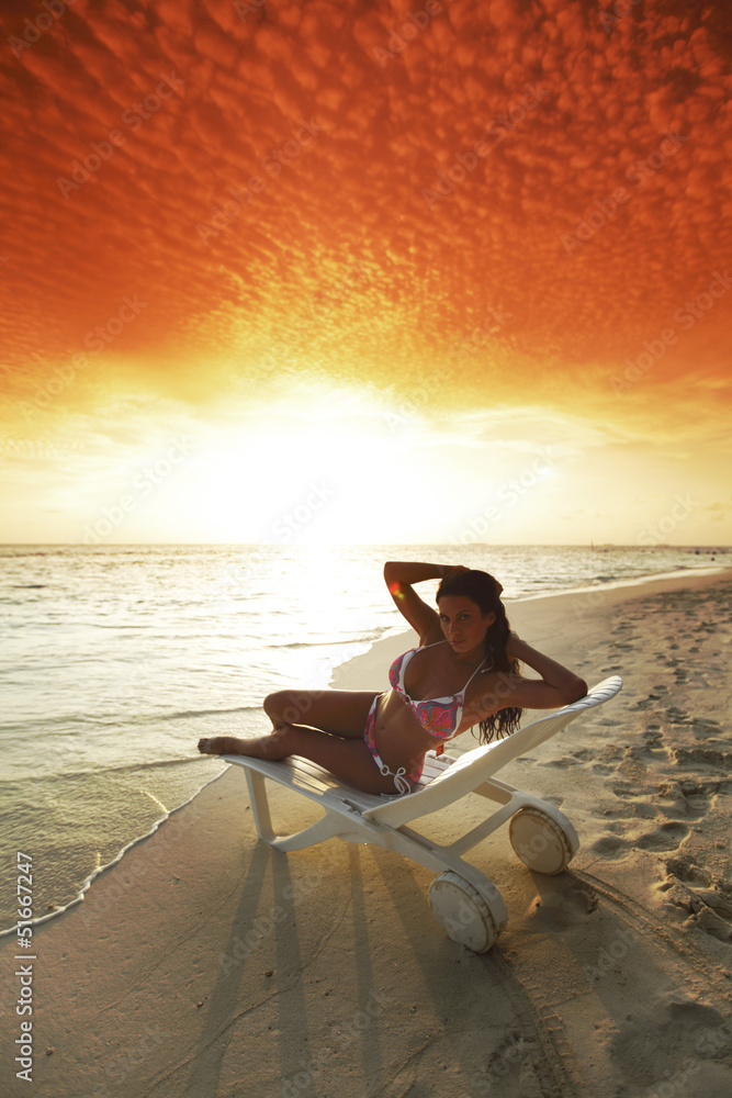 Woman in chaise-lounge relaxing on beach