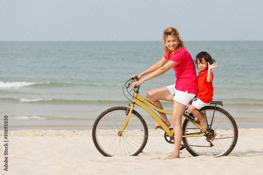 Asian son and mother riding bicycle on beach