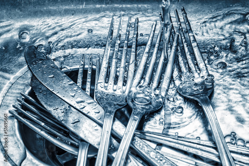Blue toned forks and knives washed on a kitchen sink