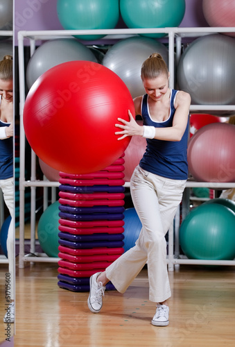 Athletic woman in sports wear exercises with red gym ball