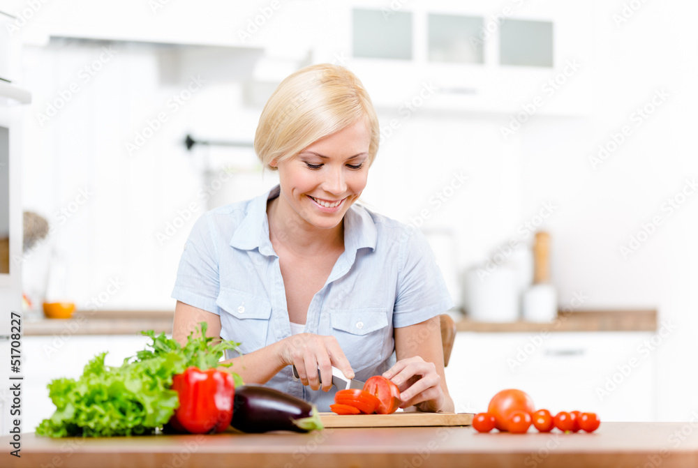 Woman cuts groceries for salad sitting at the kitchen