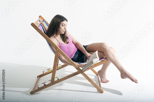 Young woman sitting on a deckchair reading book