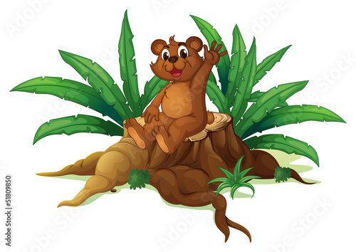 A bear waving its hand while sitting above a chopped wood