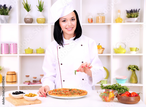 Beautiful girl chief-cooker with pizza on kitchen background