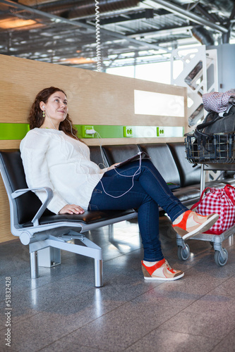 Woman dreaming with pc in airport lounge with luggage cart