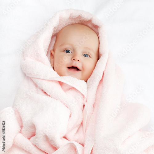Caucasian baby boy covered with pink towel joyfully smiles at ca © Maygutyak