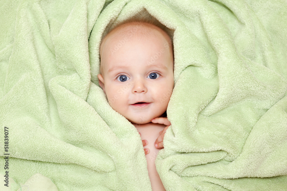Caucasian baby boy covered with green towel joyfully smiles at c Caucasian baby boy covered with green towel joyfully smiles at c