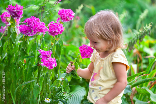 Cute little girl sitting among the flowers. Sunny summer day © Andrew Mayovskyy