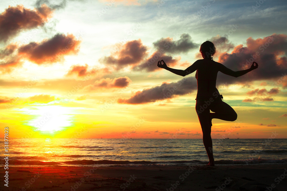 Young woman practicing yoga on the beach during sunset.