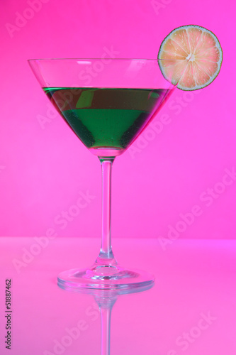 Green cocktail in martini glass on pink background
