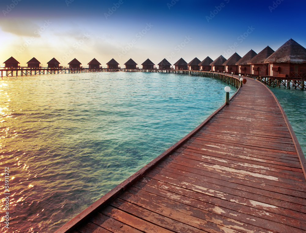 Island in ocean, overwater villas at the time sunset.