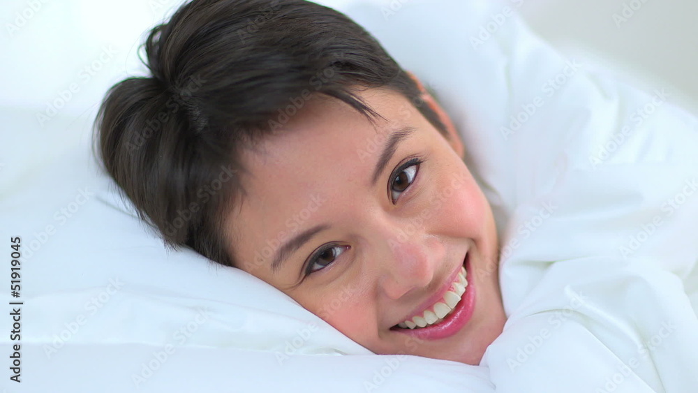 Mixed race Asian woman smiling under sheets in bed Mixed race Asian woman smiling under sheets in bed
