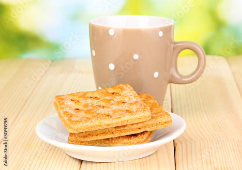 Cup of tea and cookies on wooden table on bright background