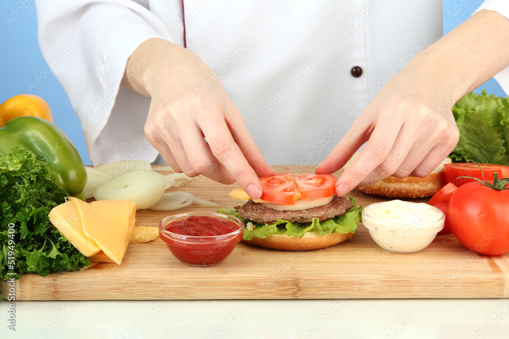 Female hands preparing cheeseburger, on blue background Female hands preparing cheeseburger, on blue background
