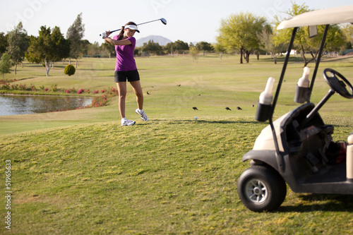 Cute female golfer swinging the ball next to a golf cart