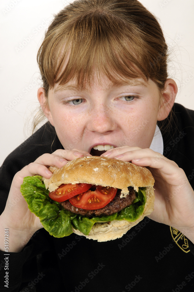 Schoolgirl eating a beefburger with a healthy salad filling Schoolgirl eating a beefburger with a healthy salad filling