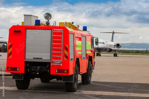 Red airport fire truck driving on tarmac by the airplane photo