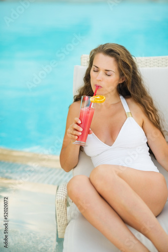 Young woman laying on chaise-longue and drinking cocktail