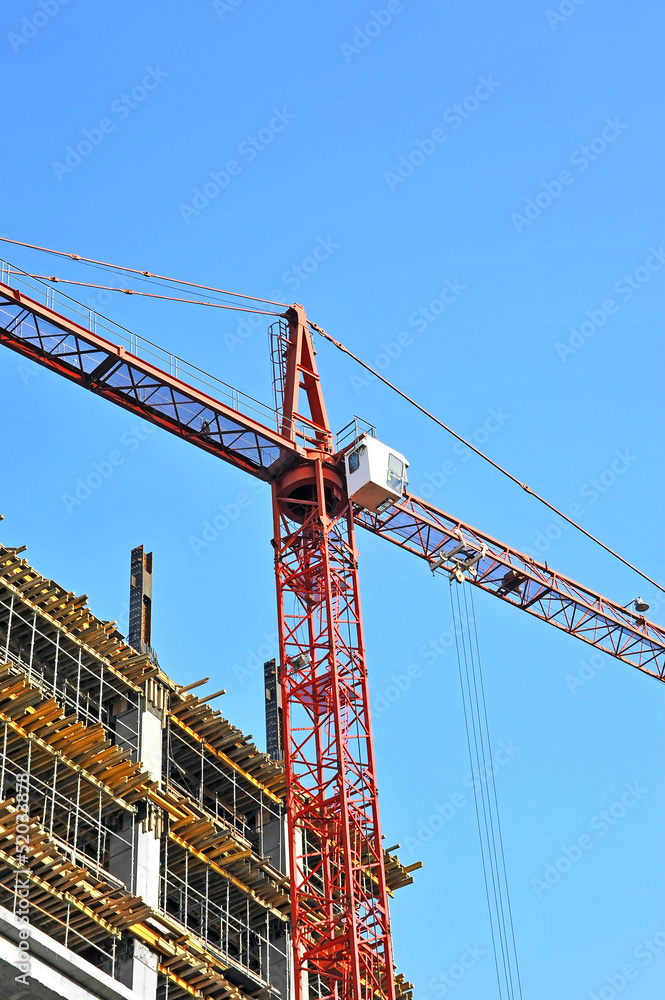 Building crane and building under construction against blue sky