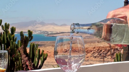 Filling a glass with water. Fuerteventura coast on background