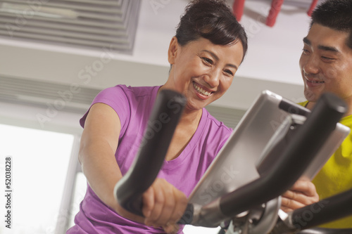Woman smiling and exercising on the exercise bike with her trainer