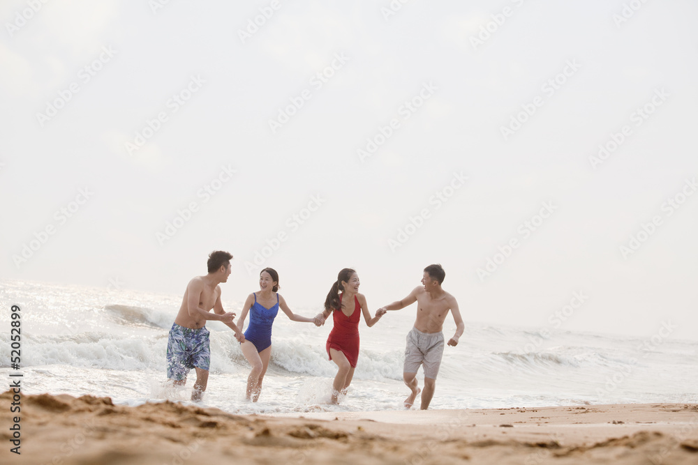 Four friends running out of the water on a sandy beach Four friends running out of the water on a sandy beach