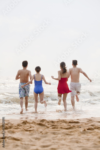 Four friends running into the water on a sandy beach