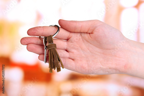 Key with leather trinket in hand on bright background