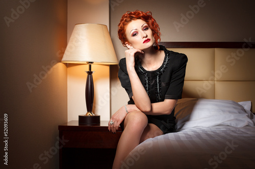 Attractive young adult woman sitting on bedside table in hotel