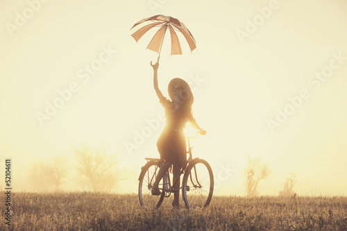 Girl with umbrella on a bike in the countryside in sunrise time #52104611