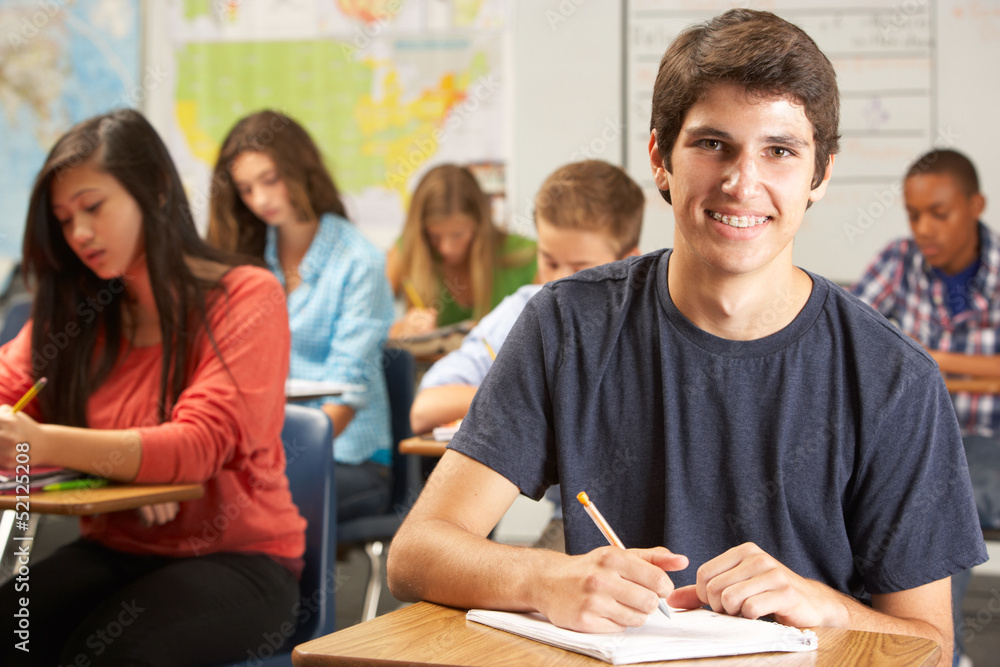 Portrait Of Male Pupil Studying At Desk In Classroom Portrait Of Male Pupil Studying At Desk In Classroom