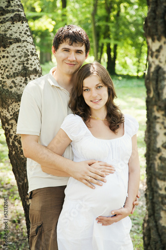 Pregnant wife and her husband in park next to trees © liubomirt