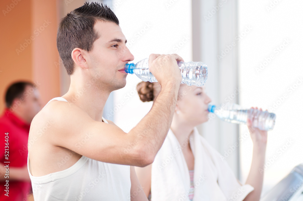 Man and woman drinking water after sports in gym Man and woman drinking water after sports in gym