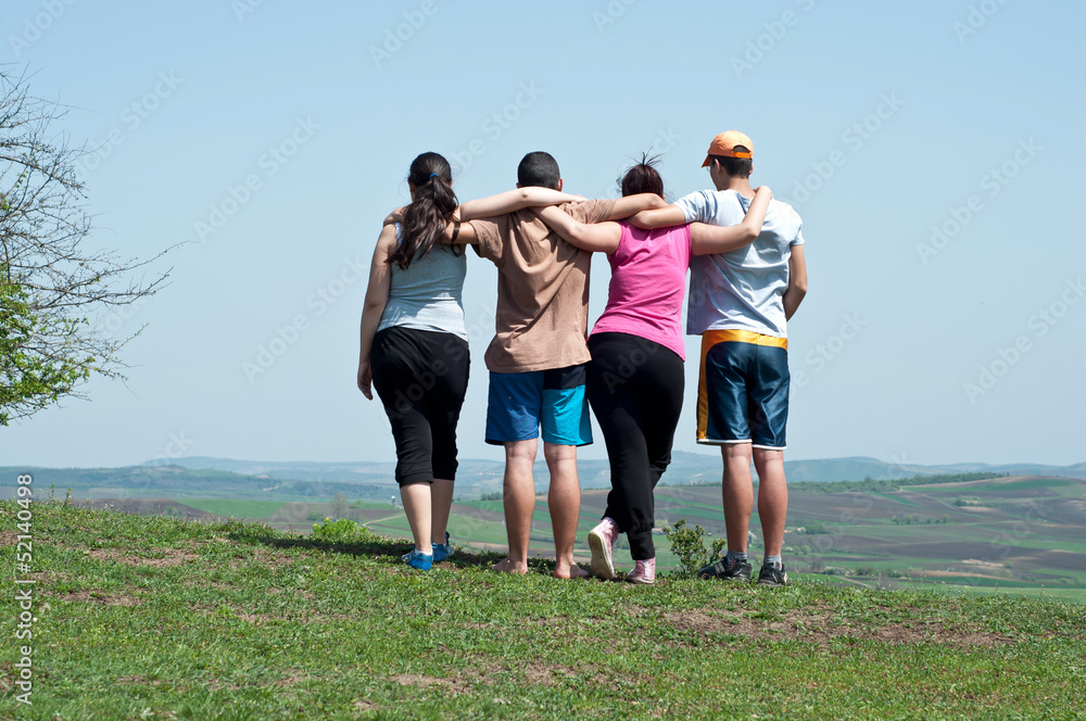 Four happy teenage friends embracing on blue sky background Four happy teenage friends embracing on blue sky background