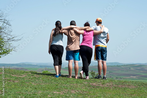 Four happy teenage friends embracing on blue sky background