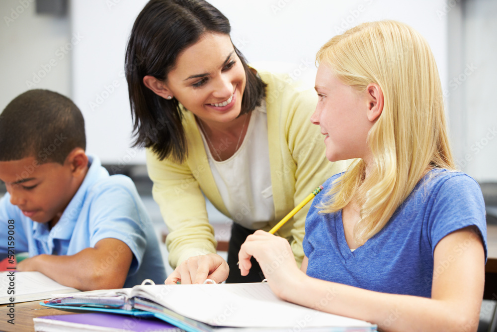 Teacher Helping Pupils Studying At Desks In Classroom Teacher Helping Pupils Studying At Desks In Classroom