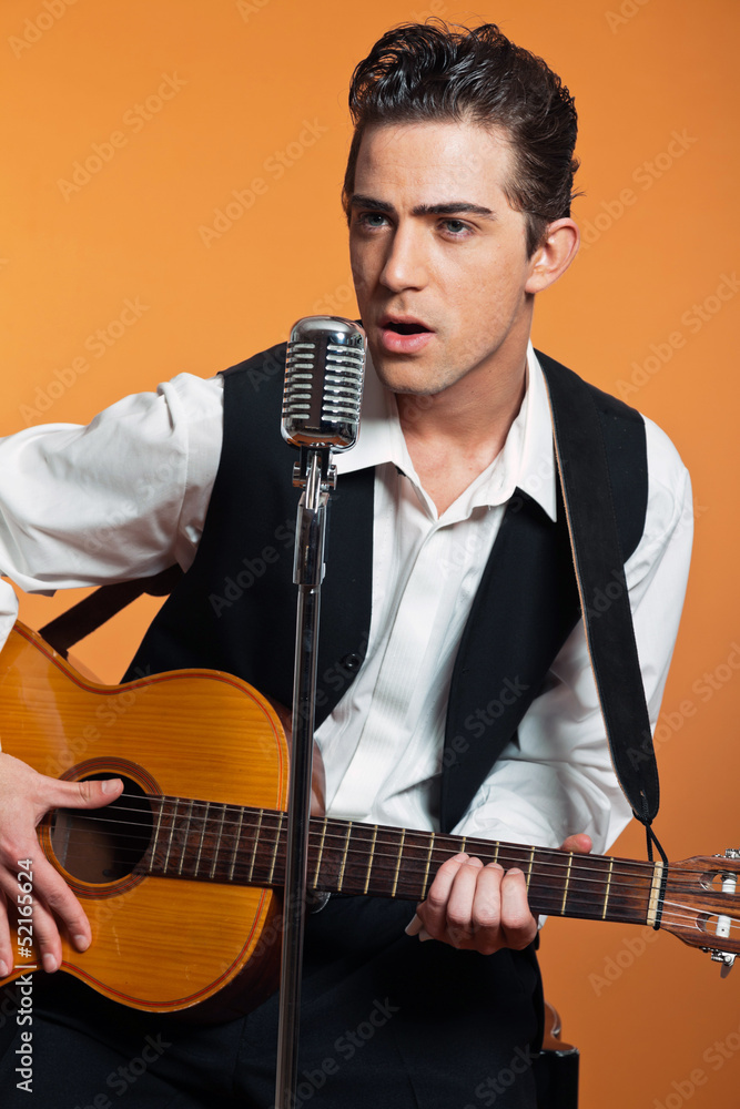 Naklejka premium Retro country singer with guitar wearing black suit. Studio shot