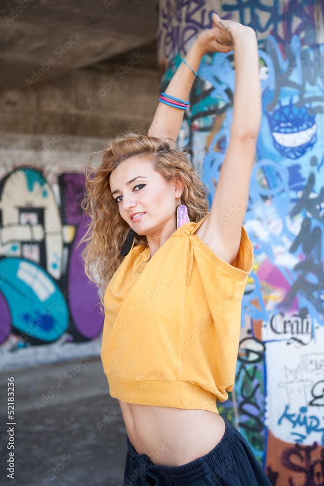 Beautiful hip teenage blonde woman stretching by graffiti wall