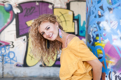 Happy hip teenage blonde girl standing by graffiti wall