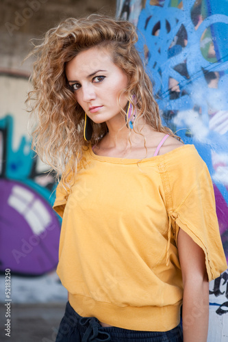 Beautiful hip teenage blonde woman standing by graffiti wall