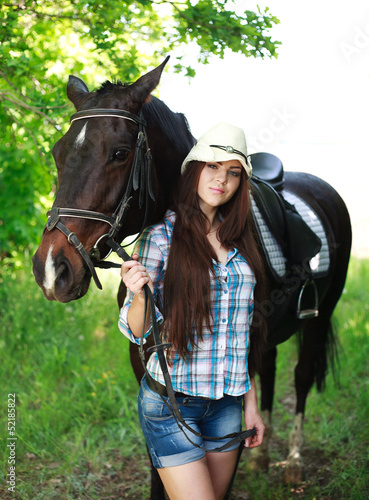 Outdoor portrait of beautiful cowgirl with horse in green