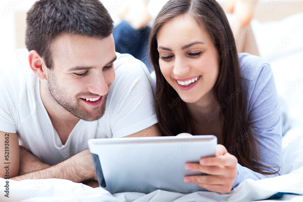 Couple with digital tablet lying on bed Couple with digital tablet lying on bed