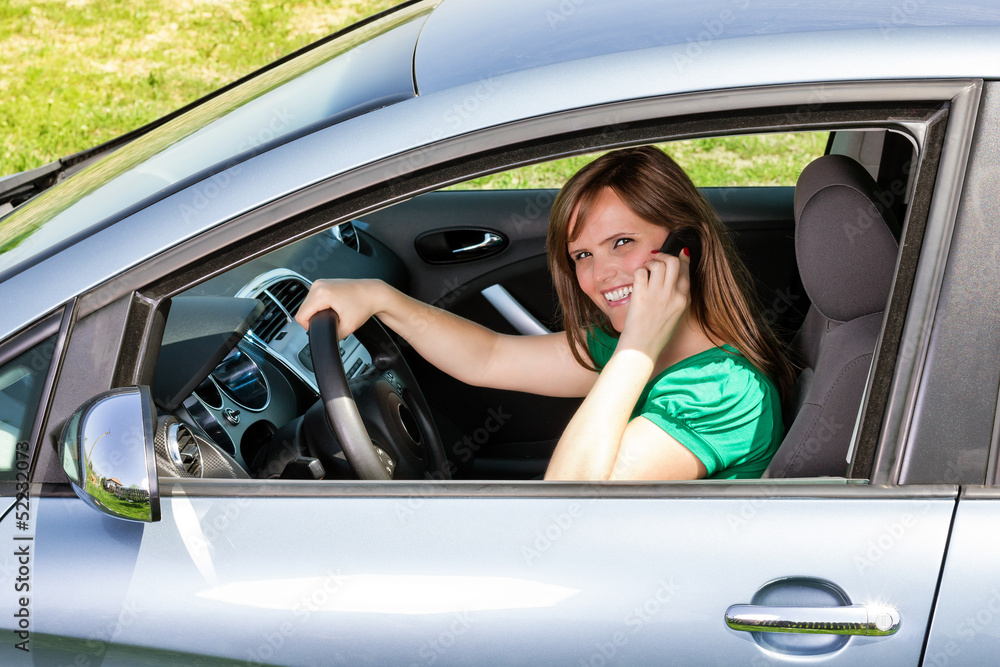 Smiling young woman using smart phone while driving