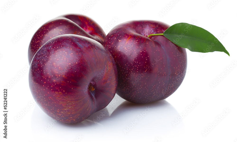 Three ripe purple plum fruits with green leaves isolated
